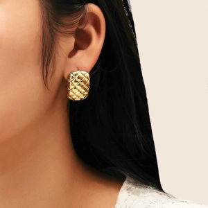 Détail d'une boucle d'oreille géométrique dorée avec motif matelassé sur un mannequin