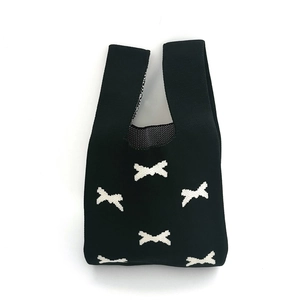 Detail shot of a black knitted bucket bag featuring white bow patterns on white background