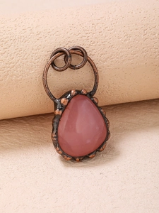 Close-up of a pink teardrop gemstone pendant set in a vintage bronze metal frame