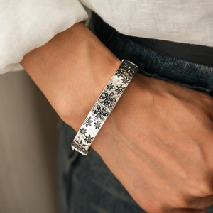 Détail d'un bracelet gravé flocon de neige en argent vintage porté avec un jean bleu
