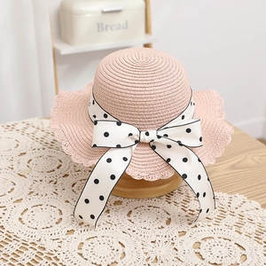 Detail of pink straw hat with wave brim and white polka dot bow on wooden stand