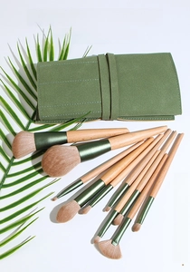 Detailed flat lay of 10-piece wood makeup brush set with green wrap bag and palm leaf