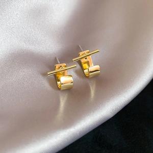 Detailed close-up of golden geometric stud earrings on elegant champagne silk fabric