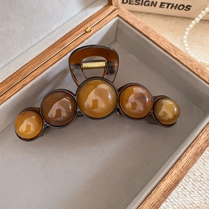 Detailed top view of amber resin geometric hair claw with five round beads in wooden box