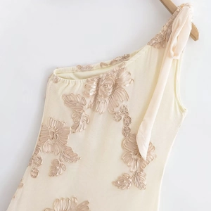 Détail de la robe beige à une épaule avec broderies florales 3D et nœud sur l'épaule