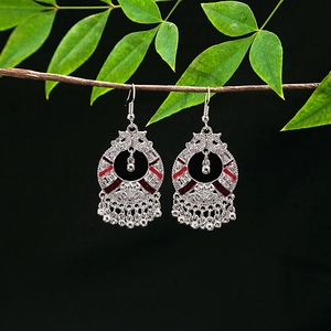 Detail view of retro silver alloy earrings with red enamel and bells on a branch