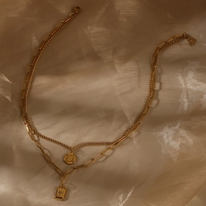 Detail of layered gold double chain necklace with starburst and square relief pendants