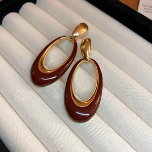 Detail of vintage gold-plated earrings with deep red oval enamel inlays on beige velvet