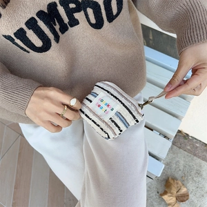 Detail of striped canvas pouch with colorful label held by model in neutral setting