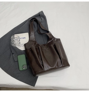 Flat lay of a large brown leather tote bag with front pockets on a grey blazer background