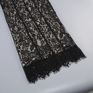 Close-up of black lace fabric with eyelash trim detail and nude lining on the dress