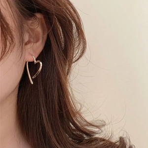 Detailaufnahme der goldenen minimalistischen Herzohrringe am Model mit Metalloberfläche