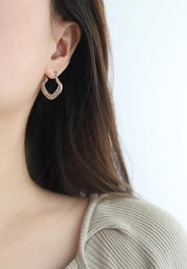 Close-up of textured silver geometric hoop earrings worn by a model in a natural setting