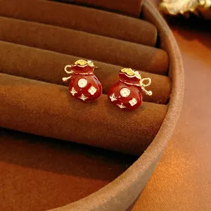 Red enamel lucky bag earrings with gold knots and white floral patterns on velvet
