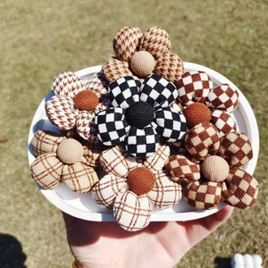 Hand holding tray of checkered fabric flower accessories for DIY crafts and hair decor