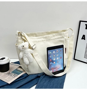 Detailed view of cream canvas messenger bag with cute bear charm and outer pocket