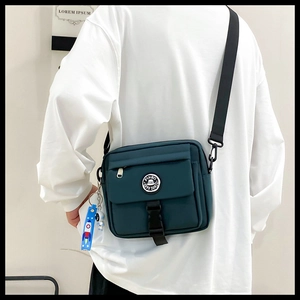 Detail view of dark green nylon messenger bag with astronaut keychain and buckle strap