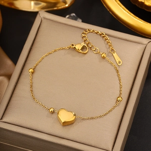 Detail view of a gold heart pendant bracelet with polished beads and lobster clasp on jewelry box