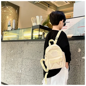 Petit garçon portant un mini sac à dos en nylon beige avec étiquette Girl Cats au café
