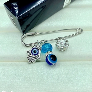 Elegant Evil Eye brooch pin with Hamsa Hand pendant and blue crystals on textured background