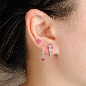 Silver snake-shaped earrings set with rose red crystals and floral studs worn on ear