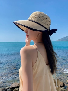 Detail of beige straw sun hat with black ribbon bow against a blue ocean background