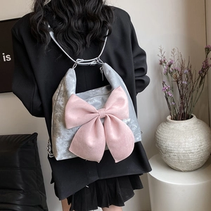 Grey velvet backpack with pink oversized bow and silver chain, worn by a model