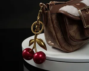 Close-up of cherry charm with red glitter on a brown monogram bag with white fleece trim