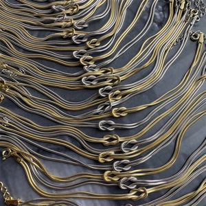 Detailed view of bulk gold and silver snake chain necklaces with central knot and lobster clasp