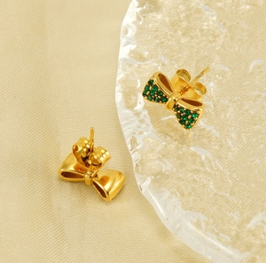 Détail de boucles d'oreilles nœud en or 18K avec cristaux verts sur lin beige texturé