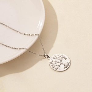 Macro shot of a silver tree of life pendant necklace on a white ceramic plate