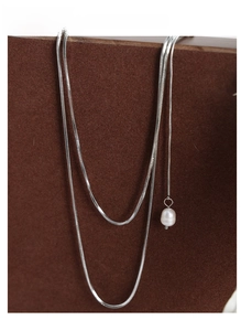 Macro shot of double-layered snake chain necklace with pearl pendant on brown texture
