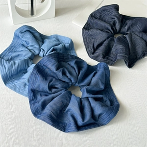 Close-up of three denim scrunchies in light blue, dark blue and black on a textured surface