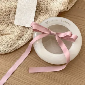 Pink satin ribbon bow hair clip displayed on an elegant white ceramic tray