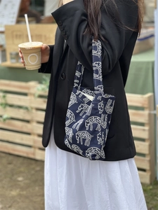 Detail of navy canvas handbag with white sheep print shown in an outdoor lifestyle setting