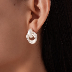 Gros plan de boucles d'oreilles nœuds argentés mats sur le modèle montrant la texture