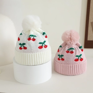 Detail of cherry jacquard pattern and fluffy pom-pom on the warm winter knitted hat