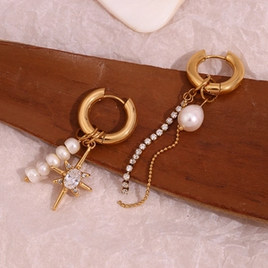 Detailed view of asymmetrical gold earrings with freshwater pearls and star charms on wood