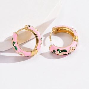 Macro detail of gold flower earrings with pink enamel and white floral patterns