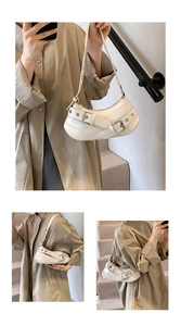 Detail of creamy white underarm bag featuring multiple silver metal belt buckle accents