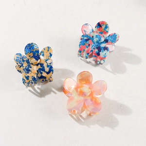 Three retro floral acrylic hair claws in assorted colors on a beige background