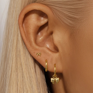 Close-up of a gold butterfly earring set with studs and hoops worn by a model