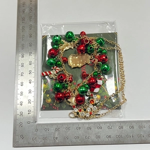 Close-up of Christmas necklace with gingerbread man and bell charms next to a ruler