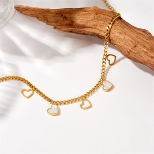 Detail of gold Cuban chain anklet featuring heart charms and white shell inlays on wood