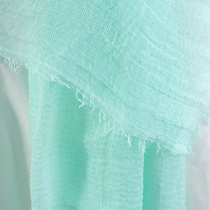 Detail of light green crinkled cotton scarf featuring soft texture and fringe edges