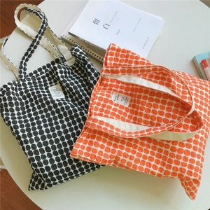 Close-up of canvas tote bags with black dots and orange plaid patterns on a table