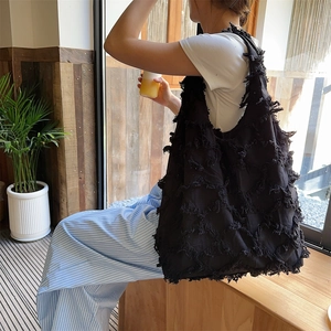 Close-up of a large black canvas tote bag featuring textured fringe and tassel details