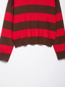 Detail showing the red and brown striped knit pattern and ribbed hem of the polo sweater