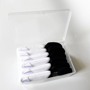 Clear storage box containing ten black and white velvet makeup sponges with ribbon handles