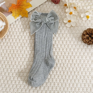 Detail of grey knitted baby knee-high socks with a large velvet bow on a cozy background